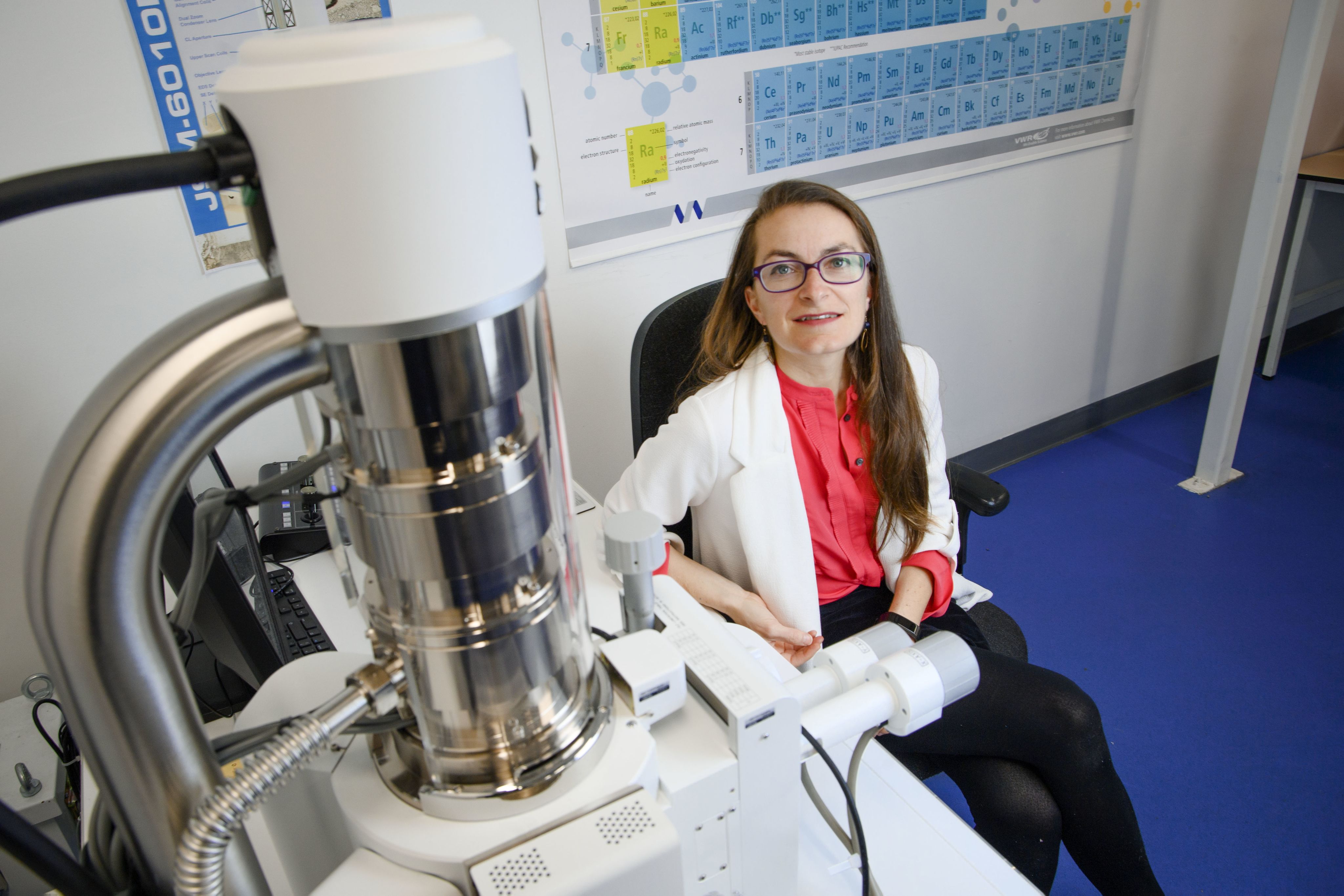 An academic looking at camera with periodic table behind her